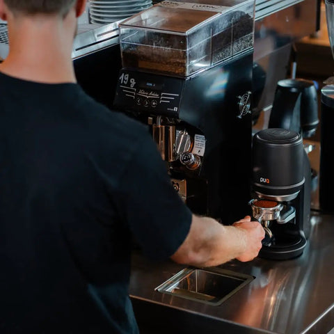 Electric Auto Leveling Espresso Tamper For 57.3 Mm Portafilters in use at a coffee counter with grinder and espresso machine