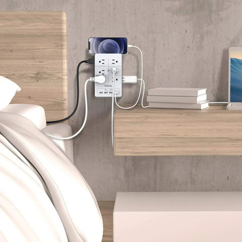 2 Pack Surge Protector Power Strip With 4 USB Ports mounted on wall, charging devices on a bedside table.