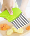 Crinkle cutter with green handle and stainless steel blade, held in hand over sliced carrots and potatoes.