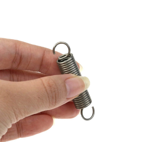 Close-up of two small stainless steel extension springs with dual hooks, 0.4x2 in, held between fingers
