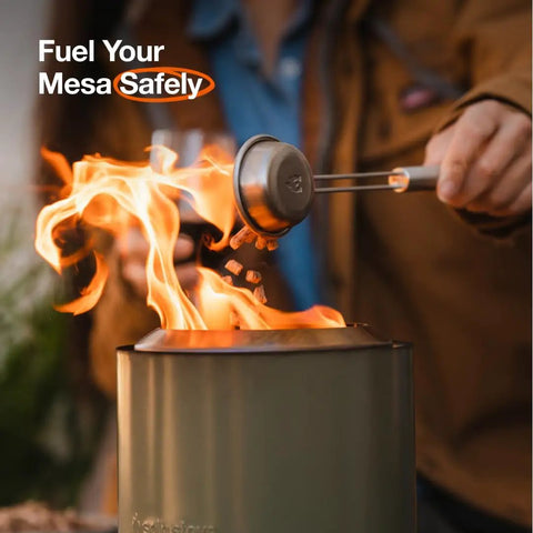 Person using pellet scoop from Mesa Outdoor Fire Pit Accessory Pack With 4 Stainless Steel Mini Sticks Stick Rests Pellet Scoop Lid And Carry Case Essential Gear To Amp Up Your Tabletop Fire Pit Party And Keep The Night Lit next to tabletop fire pit.