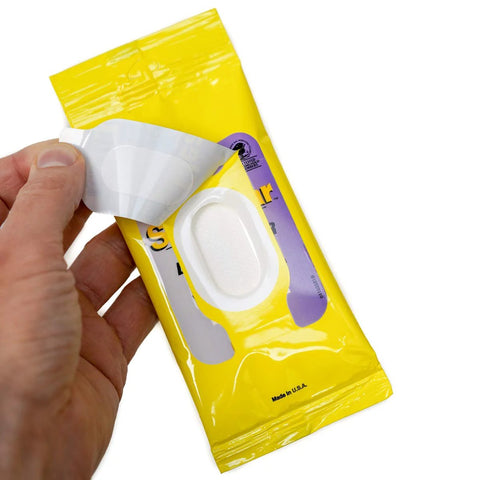 Front view of See Clear Original Lens Cleaning Wipes package; hand lifts a white pre-moistened wipe from a yellow resealable pouch.