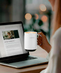 Smart Self Heating Coffee Mug With AI Temp Control And 20 Oz Capacity being held next to a laptop with steam rising from the drink.