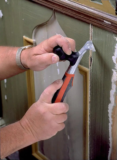 Heavy Duty Carbide Blade Scraper With 2.5 Inch Wide Blade removing paint from wooden panel, ergonomic handle visible