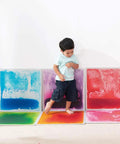 Child stepping on Six Assorted Color 12 by 12 Inch Liquid Floor Tiles Set for Kids, Kid Friendly Sensory Floor Tiles Where Color Flows With Every Step.