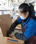 Worker in protective gear packaging a product into a cardboard box in a factory setting
