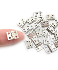 Miniature Brass Hinges Set For Jewelry Boxes And Cabinets 24 Pieces 10 By 8 Millimeter silver finish shown next to finger