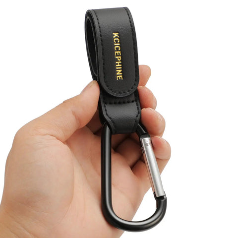 Hand holding one of the 2 Pack Universal Stroller Hooks with Adjustable Carabiner Clips For Diaper Bags And More, Durable Matte Black Hardware.