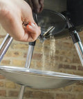 Hand operating the One-Touch Cleaning System on Original Kettle Charcoal Grill 22-Inch Black for ash removal in backyard BBQs