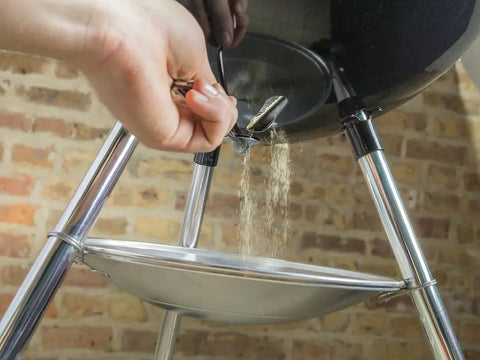 Hand operating the One-Touch Cleaning System on Original Kettle Charcoal Grill 22-Inch Black for ash removal in backyard BBQs
