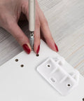 Person using a screwdriver to install a Slick White Plastic Drawer Track Guide Kit Packing 10 Pieces on a white board.