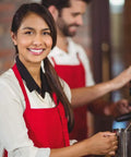 Smiling woman wearing Bulk Pack Bib Aprons For Restaurant Pros, 12 Pack, Long Oversized Unisex Kitchen Aprons, red, at a café.