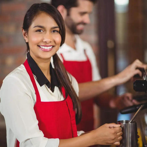 Smiling woman wearing Bulk Pack Bib Aprons For Restaurant Pros, 12 Pack, Long Oversized Unisex Kitchen Aprons, red, at a café.
