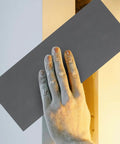 Hand holding grey sanding paper against a wall, demonstrating Premium 21 Piece Grit Wet Dry Sanding Paper Sheets for projects.