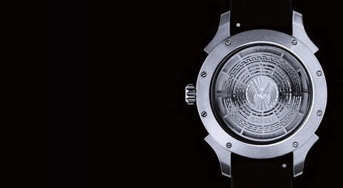Back view of a luxury watch showcasing detailed casing, "Inside The World Of Masterful Watchmakers A Luxe No Nonsense Look At Timeless Craft..."