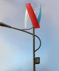 Vertical axis wind turbine with three blades in red, white and blue atop a metal pole.