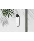 Nest Doorbell Battery Snow Finish With HD Live View, HDR And Night Vision mounted on a white wall with a plant shadow