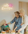 Hello Beautiful Neon Sign For Girl's Room Wall Decor With Dimmer Switch Romantic Neon Light For Weddings Valentine's Day Parties Gifts 12V Warm White With Power Adapter Included glowing on wall above three women seated at table