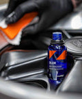 CARPRO DLUX wheel and trim coat bottle; blue glass container with orange label on a car panel.