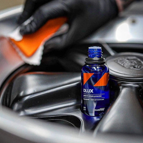 CARPRO DLUX wheel and trim coat bottle; blue glass container with orange label on a car panel.