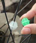 Hand placing a colorful plastic spoke bead on bicycle wheel, 36 Pack Glow In The Dark Luminous Bicycle Wheel Spoke Wrap Tubes In Colorful Plastic For Spokes Decoration Bike Accessories That Spruce Up Your Ride With Eye Catching Colors.