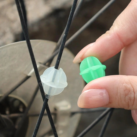 Hand placing a colorful plastic spoke bead on bicycle wheel, 36 Pack Glow In The Dark Luminous Bicycle Wheel Spoke Wrap Tubes In Colorful Plastic For Spokes Decoration Bike Accessories That Spruce Up Your Ride With Eye Catching Colors.