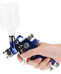 Pro Grade Mini Pneumatic Spray Gun With Swappable 0.8 And 1.0 Mm Tips for precise use, held in hand, clear fluid container attached.