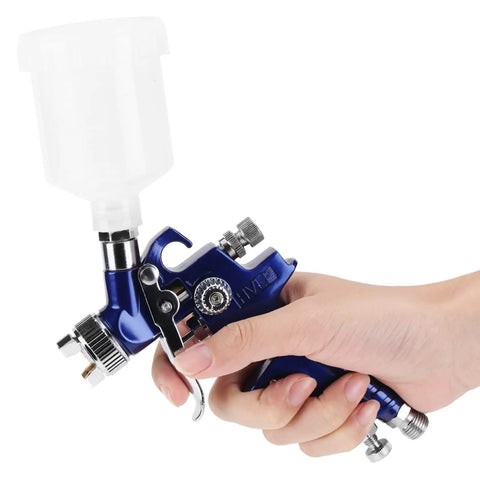 Pro Grade Mini Pneumatic Spray Gun With Swappable 0.8 And 1.0 Mm Tips for precise use, held in hand, clear fluid container attached.