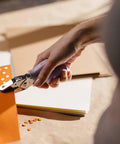 Person using Purple Circle Hand Punch 1/4 Inch for Crafts with Cushioned Grip to punch holes in orange cardstock for scrapbooking.