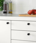 Matte Black Cabinet Knobs Four Pack With Wide Backplates on white kitchen drawers next to sliced tomatoes and condiments