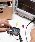 Hands using an Uno R4 WiFi Dual Core Microcontroller Board with Renesas RA4M1 and ESP32 S3 for IoT and Embedded Projects, connected to oscilloscope.