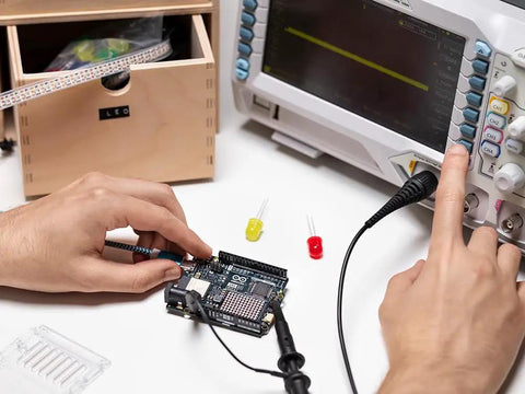 Hands using an Uno R4 WiFi Dual Core Microcontroller Board with Renesas RA4M1 and ESP32 S3 for IoT and Embedded Projects, connected to oscilloscope.