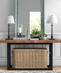Modern console table with wicker basket beneath, two blackened bronze table lamps on wooden top, white French drum shades.