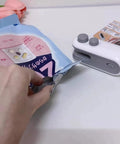 2 In 1 Portable Bag Sealer And Cutter With Rechargeable Battery in use sealing a snack bag, compact handheld design, white with gray buttons