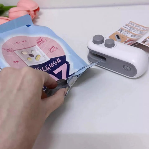 2 In 1 Portable Bag Sealer And Cutter With Rechargeable Battery in use sealing a snack bag, compact handheld design, white with gray buttons
