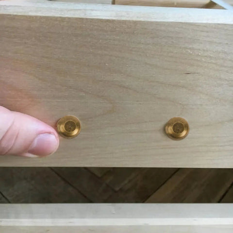 Top Shelf Brass Decorative Screws With Caps For Cabinet Doors And Wood Furniture on a wooden surface, showing two brass caps.