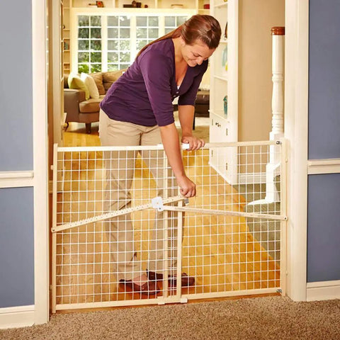 Woman adjusting extra wide wooden baby gate with wire mesh for doorways pressure mounted adjustable from about 29 to 50 inches wide and 31 inches tall