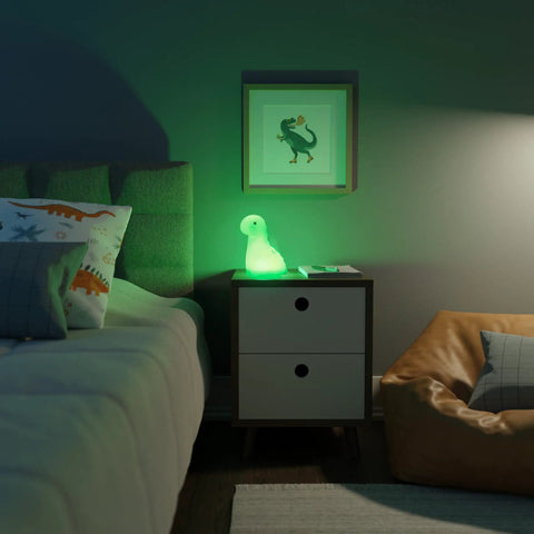 Multicolor LED Silicone Night Light Brontosaurus Tap Light For Kids Nursery Decor Rechargeable Color Changing Soft BPA Free Body Cozy Sleep Glow Bedtime Routine on bedside table, emitting green glow, in dark room.