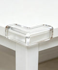 Close-up of clear PVC corner protector on white table corner, part of 4 Pack PVC Corner Protectors For Furniture With Adhesive Backing Thickened Soft Edge Bumpers For Tables Desks And Cupboards Easy Install Kidproof Safety Guards To Minimize Injuries For Active Homes