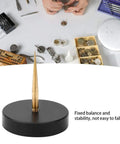 Pro Grade Watch Balance Holder for precise balance correction, black round base with gold prong, watchmaking tools in background