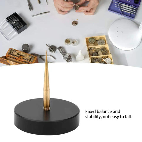 Pro Grade Watch Balance Holder for precise balance correction, black round base with gold prong, watchmaking tools in background