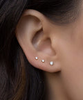 Close-up of a woman's ear with three diamond stud earrings in a graduated size.