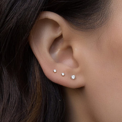 Close-up of a woman's ear with three diamond stud earrings in a graduated size.