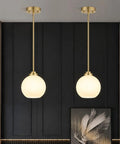 Two Pack Brushed Gold Globe Pendant Lights With Mid Century Modern Vibes And Smooth Opal Glass Shades, hanging above a modern wall.
