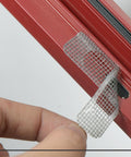 Applying 60 Pcs Window Screen Repair Patches Kit With Heavy Duty Adhesive Mesh Tape on red window frame for tear repair