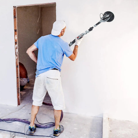 Man using Powerful 710W Drywall Sander With LED Light And Variable Speed 800 To 1800 RPM on a wall. Focus on tool and dust hose.