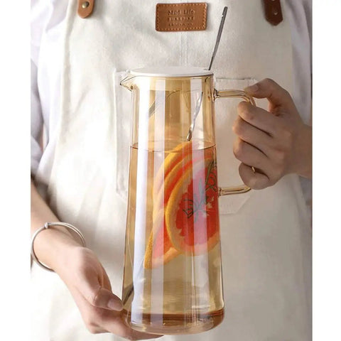 A Game Changer High Borosilicate Glass Pitcher With Secure Tight Lid And Long Mixing Spoon One Point Six Liter heat resistant beverage carafe holding iced tea and fruit slices.