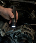 Hand using Strion HL 615 Lumen Rechargeable Pro Flashlight for engine inspection, showing LED light illuminating car parts