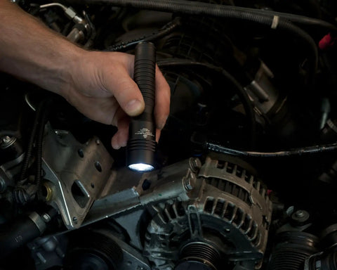 Hand using Strion HL 615 Lumen Rechargeable Pro Flashlight for engine inspection, showing LED light illuminating car parts