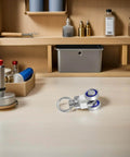 Workbench with tools and chemical bottles, small metal bearings on surface in front, organized shelves in background.